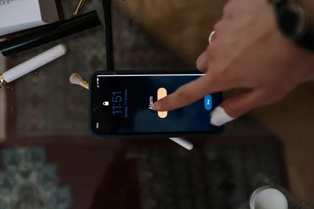 Close-up of a person touching a smartphone alarm screen with makeup items nearby. Alarmregeln nach wiederholten Fehlmeldungen bereinigen