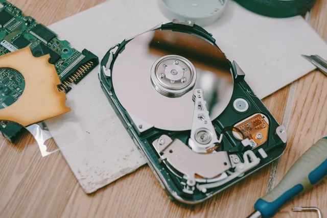 Close-up of a disassembled hard drive showing internal components on a wooden table. Eine Synchronisierung nach längerer Störung wiederherstellen