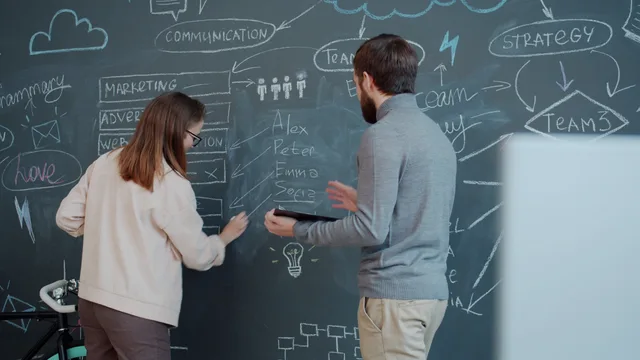 Two colleagues brainstorming a business strategy on a chalkboard with diagrams, enhancing teamwork and communication. Einen Ablauf vor der technischen Umsetzung beschreiben