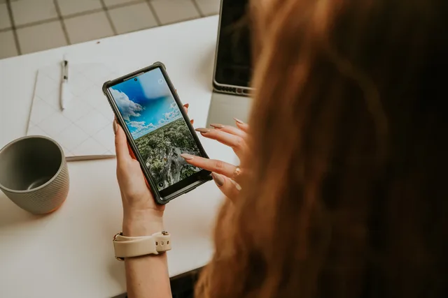 Close-up of a woman using a smartphone at a desk, indicating a modern office environment. Mobile Ansichten mit echten Aufgaben testen