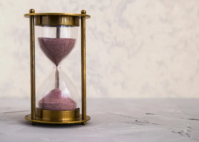 A traditional hourglass with pink sand, symbolizing time and patience on a textured surface. Unbeantwortete Freigaben auslaufen lassen